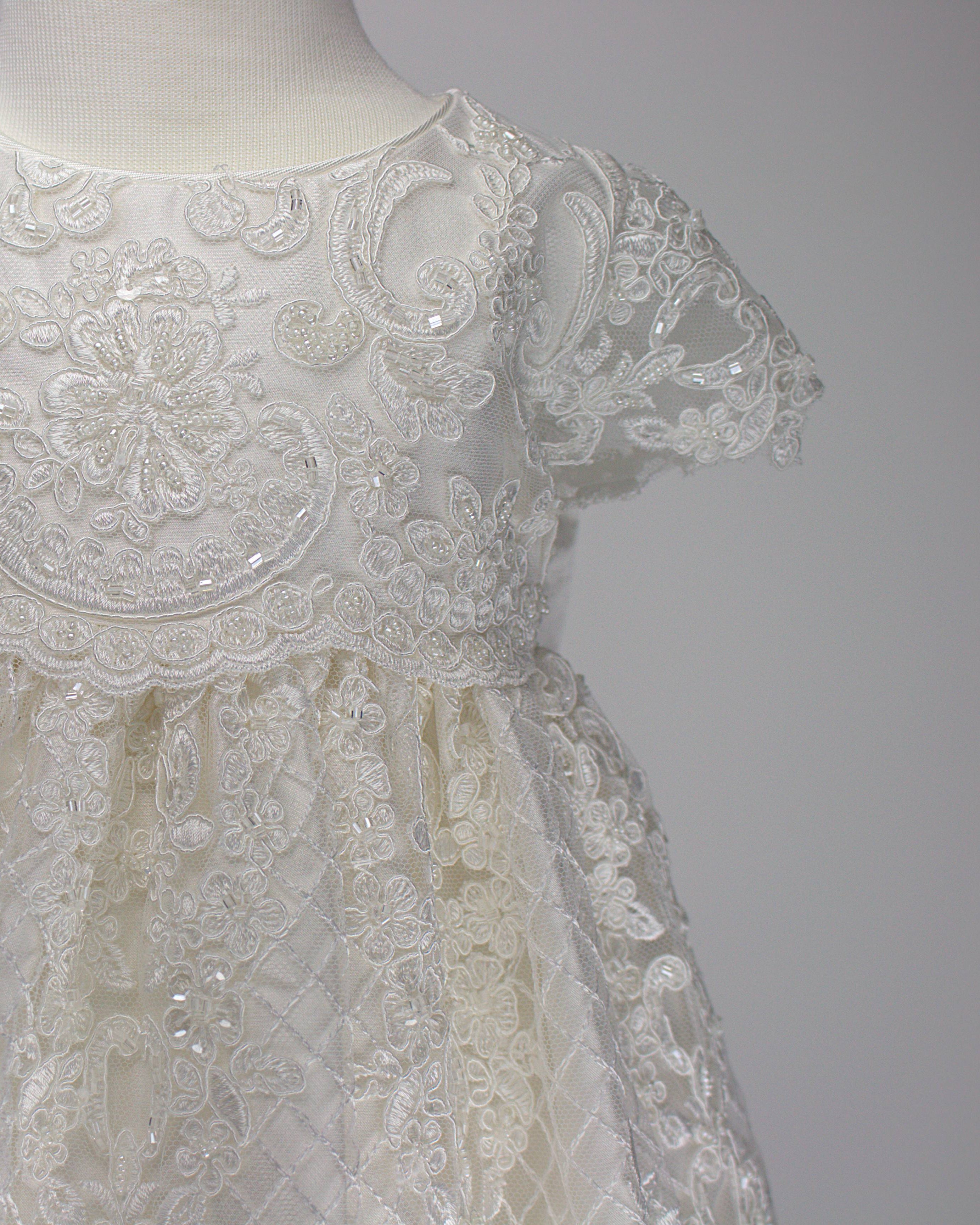 Close-up of the My Blessing Bithiah christening gown’s front bodice showing intricate floral lace embroidery layered over a smooth silk underlay.