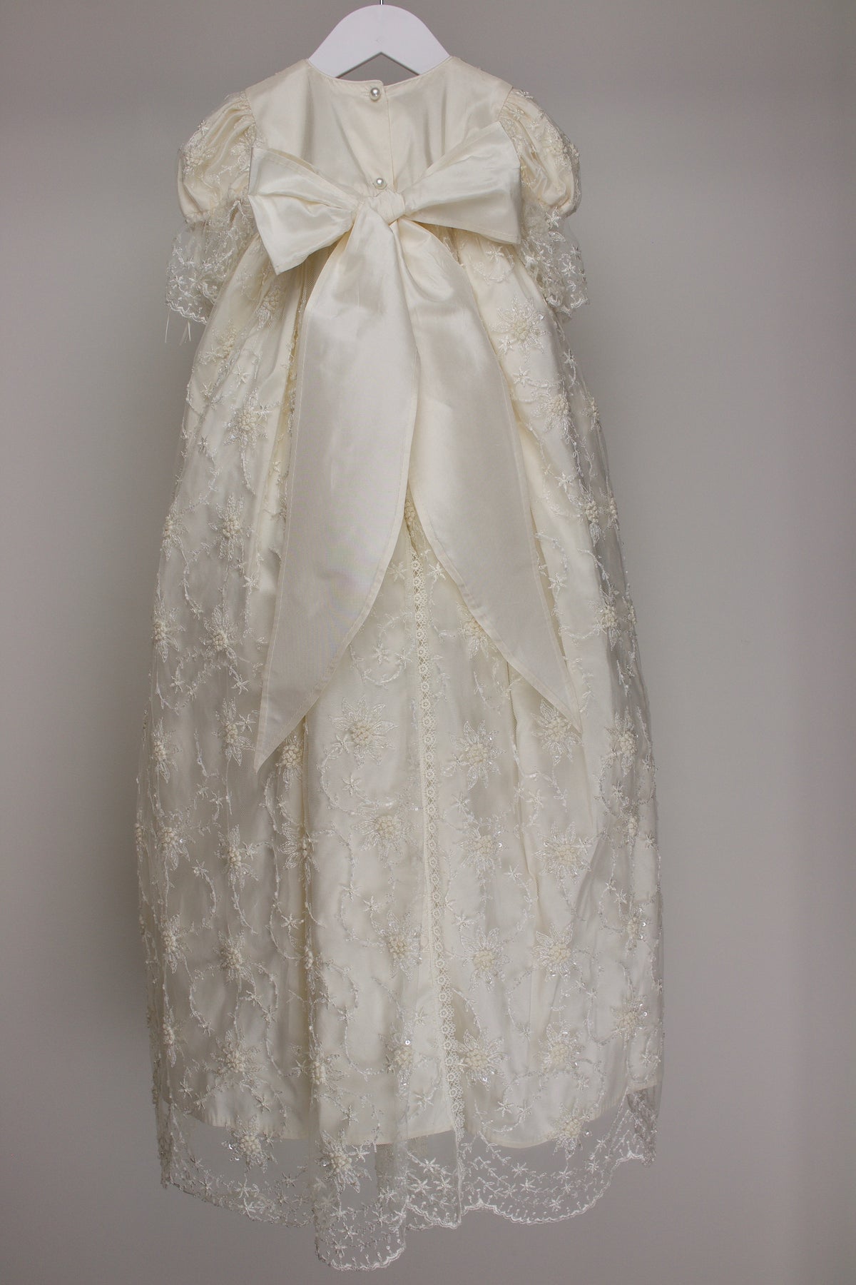 Back view of the My Blessing Devotion christening gown showing the flowing lace overlay and smooth pure silk mid‑layer.