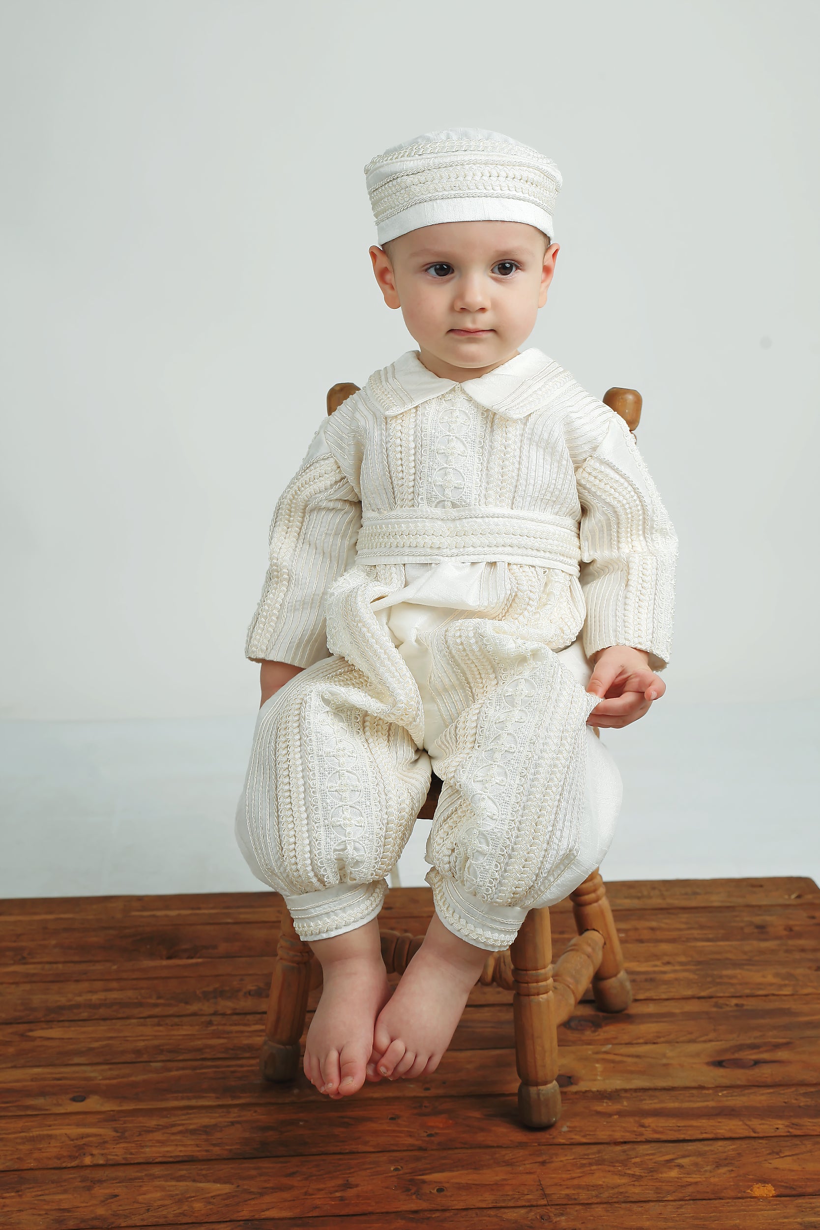 Baby boy sitting joyfully in the My Blessing Gabriel Dupioni silk romper, the hand‑finished pearl accents shimmering gently.