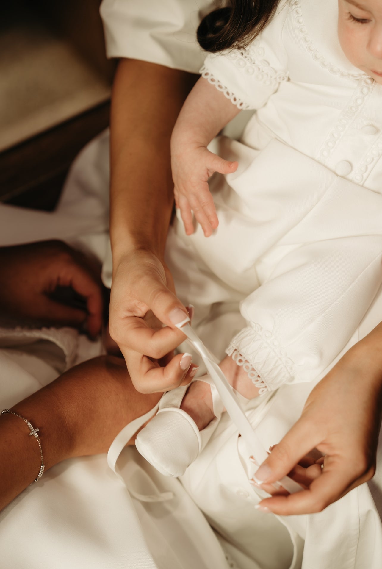 Mum tying the laces of the My Blessing Georgie Mikado shoes while baby sits patiently, the fabric glowing softly.