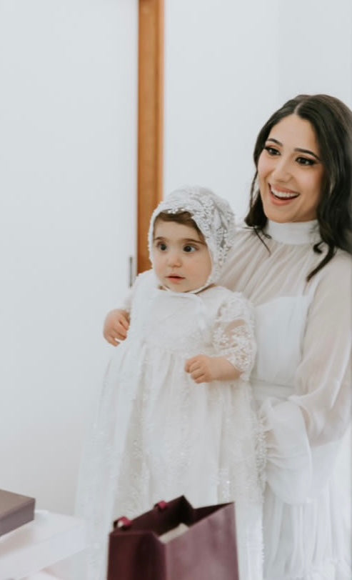 Mother holding her baby girl dressed in the My Blessing Gianna ivory christening gown, showing the embroidered lace bodice embellished with glass seed beads and pearls.