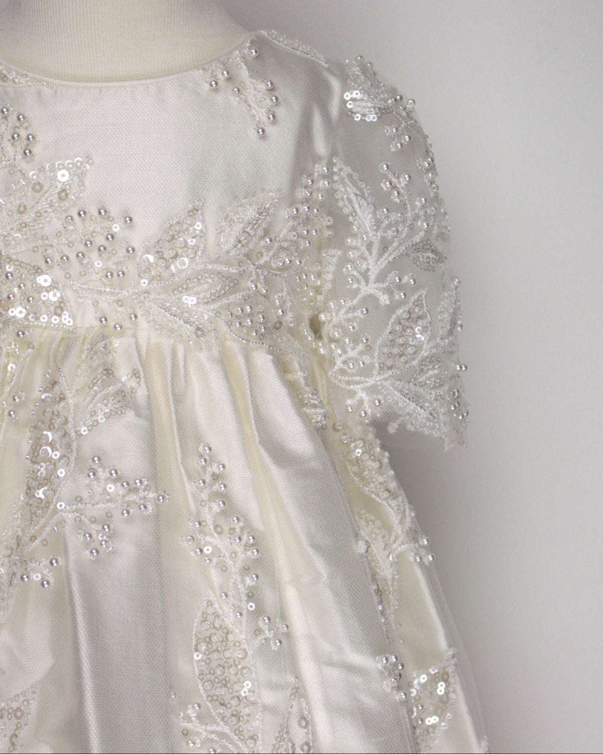 Close-up of the My Blessing Gianna christening gown’s front bodice showing intricate lace embroidery embellished with glass seed beads and pearls.