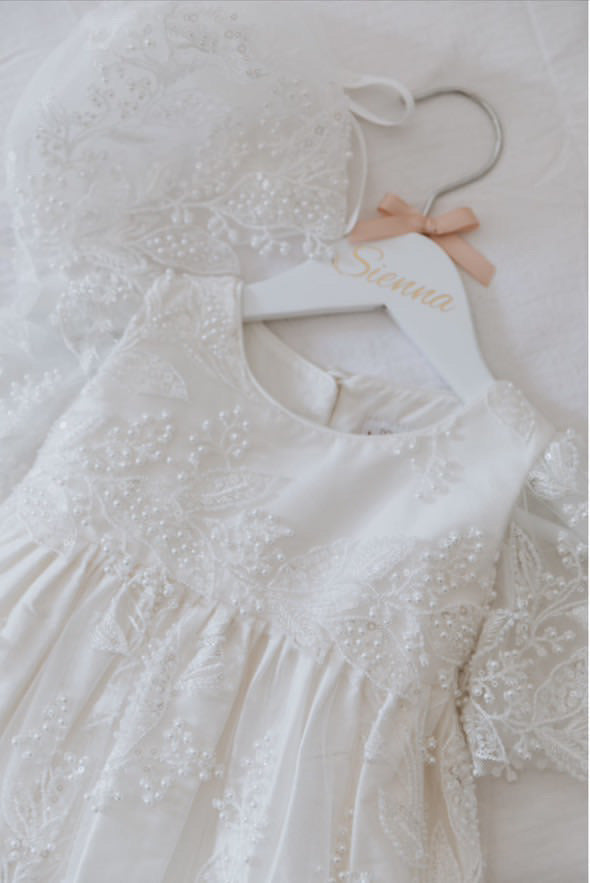 Styled flat‑lay of the My Blessing Gianna christening gown set featuring the ivory lace gown with glass seed beads and pearl embellishments, arranged with matching bonnet.