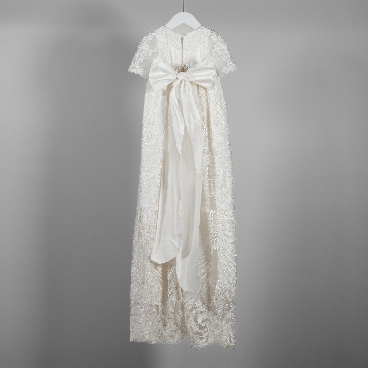 Back view of the My Blessing Psalms ivory christening gown showing lace detailing, glass seed beads, pearl detailing and a large silk bow back closures.