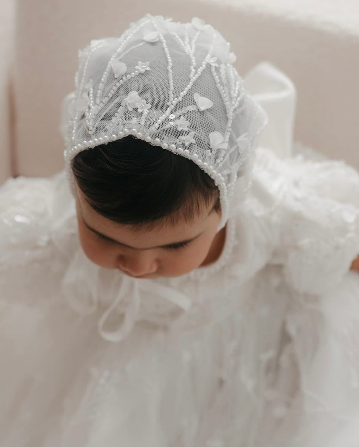 Baby wearing My Blessing Shamiran ivory christening gown with matching bonnet in a lifestyle setting, highlighting the coordinated lace details.
