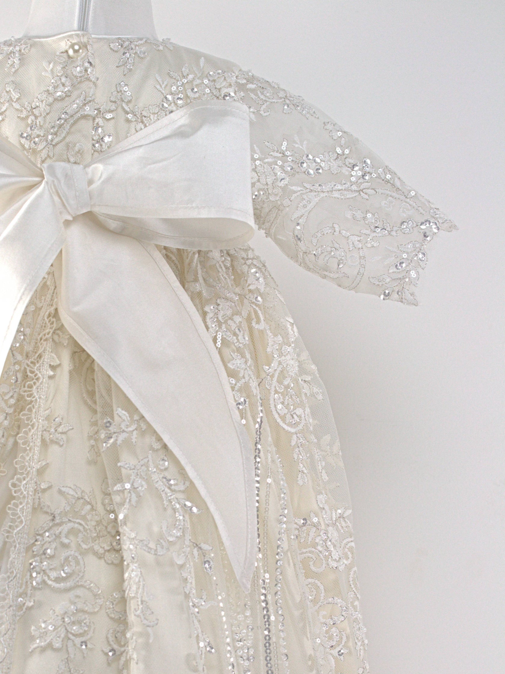 Back view of the My Blessing Wholesome ivory christening gown showing lace detailing, back closures, and the smooth satin skirt
