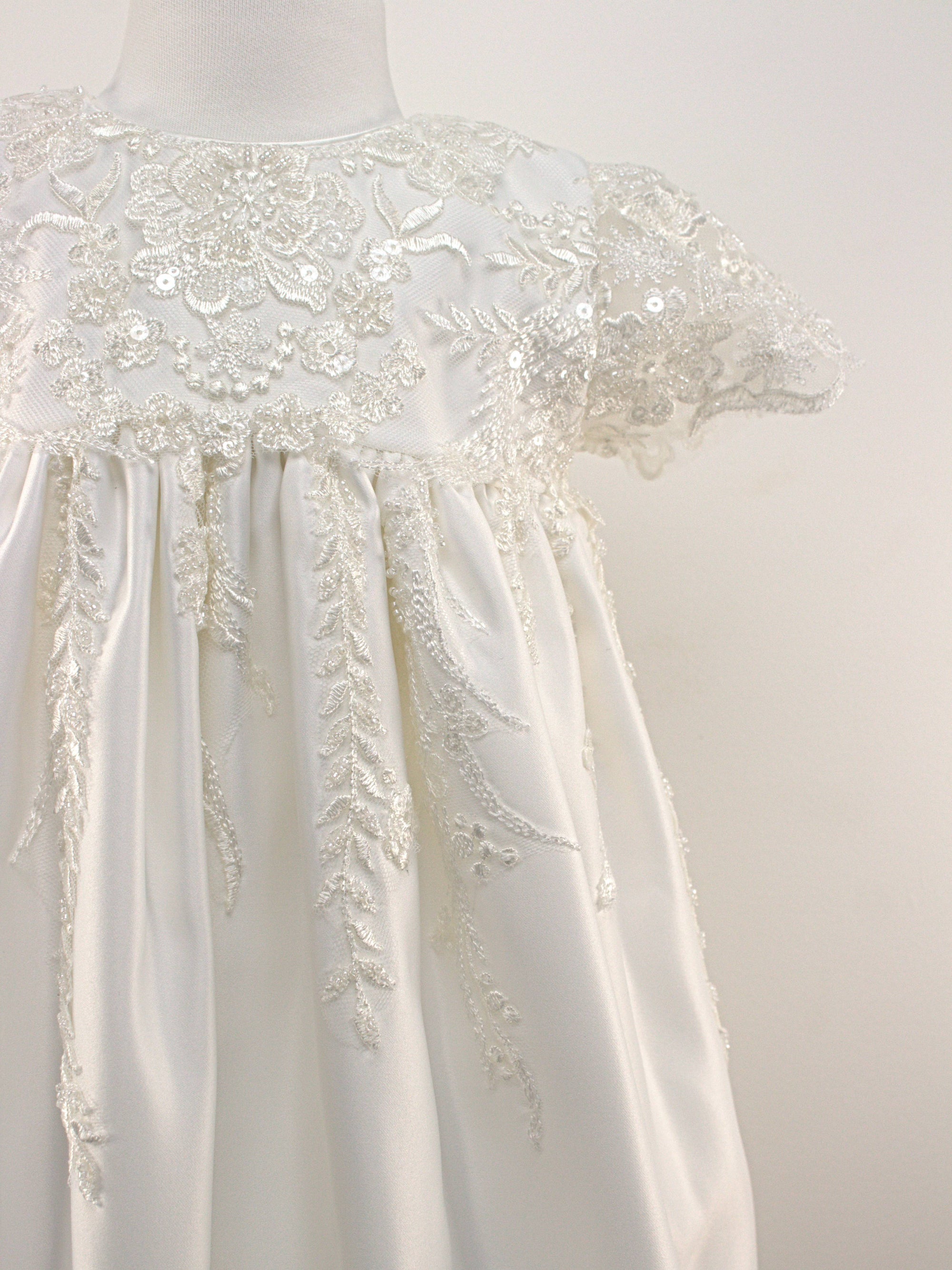 Baby christening outfit set including a long white gown with embroidered lace panels, puffed sleeves, a matching lace-trimmed bonnet, and coordinating accessories arranged neatly on a white background