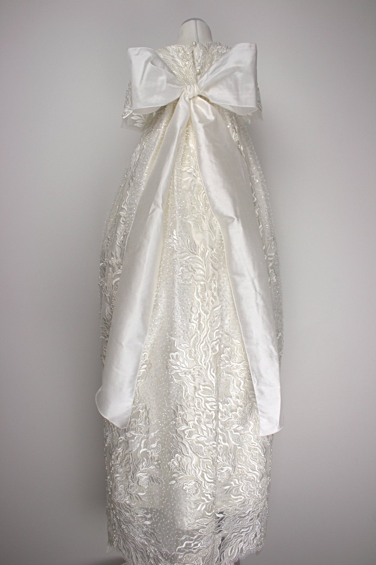 Back view of the My Blessing Zillah christening gown showing the flowing European lace overlay with shimmering Swarovski crystals, pearls, tubed glass beads, seed beads and an extra-large pure silk bow.
