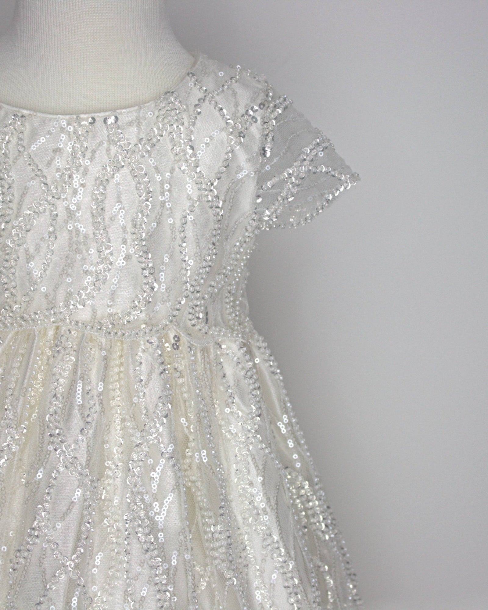 Close-up of the My blessing Zuriel christening dress’s lace bodice showing hand‑embellished floral embroidery decorated with reflective sequins and glass seed beads.