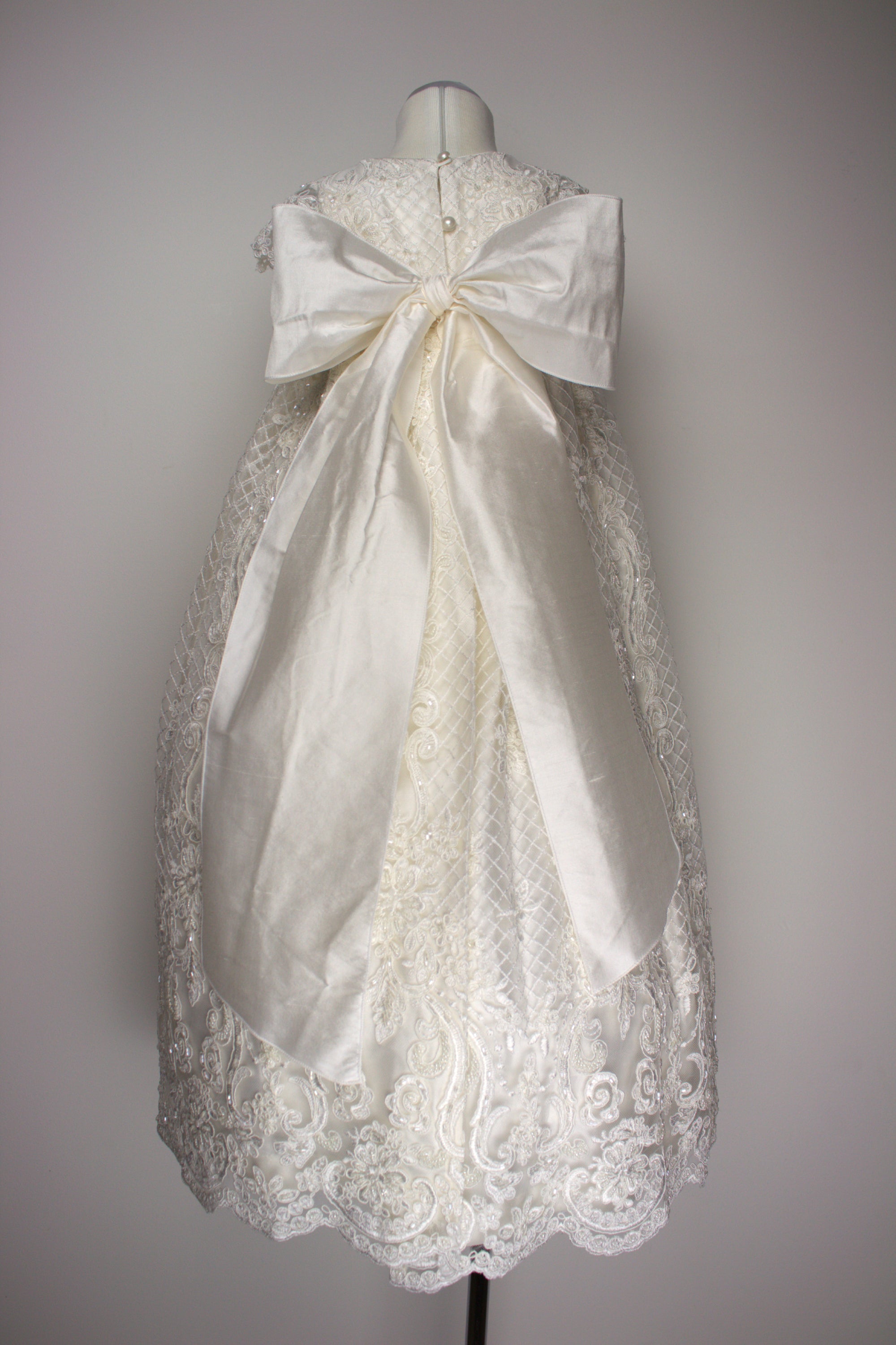 Back view of the My Blessing Bithiah ivory christening gown showing lace detailing, back closures, soft silk‑underlay skirt and large pure silk bow.