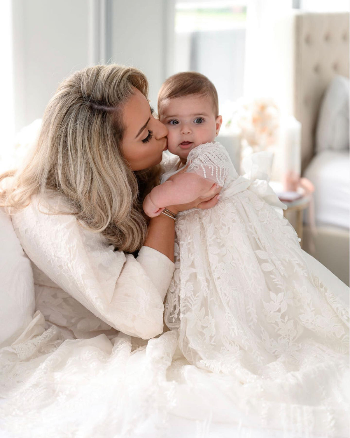 Close-up of mum kissing her baby girl in the Elora ivory gown, showing the gown’s intricate lace decorated with sequins, glass seed beads, and Swarovski crystal beadwork.