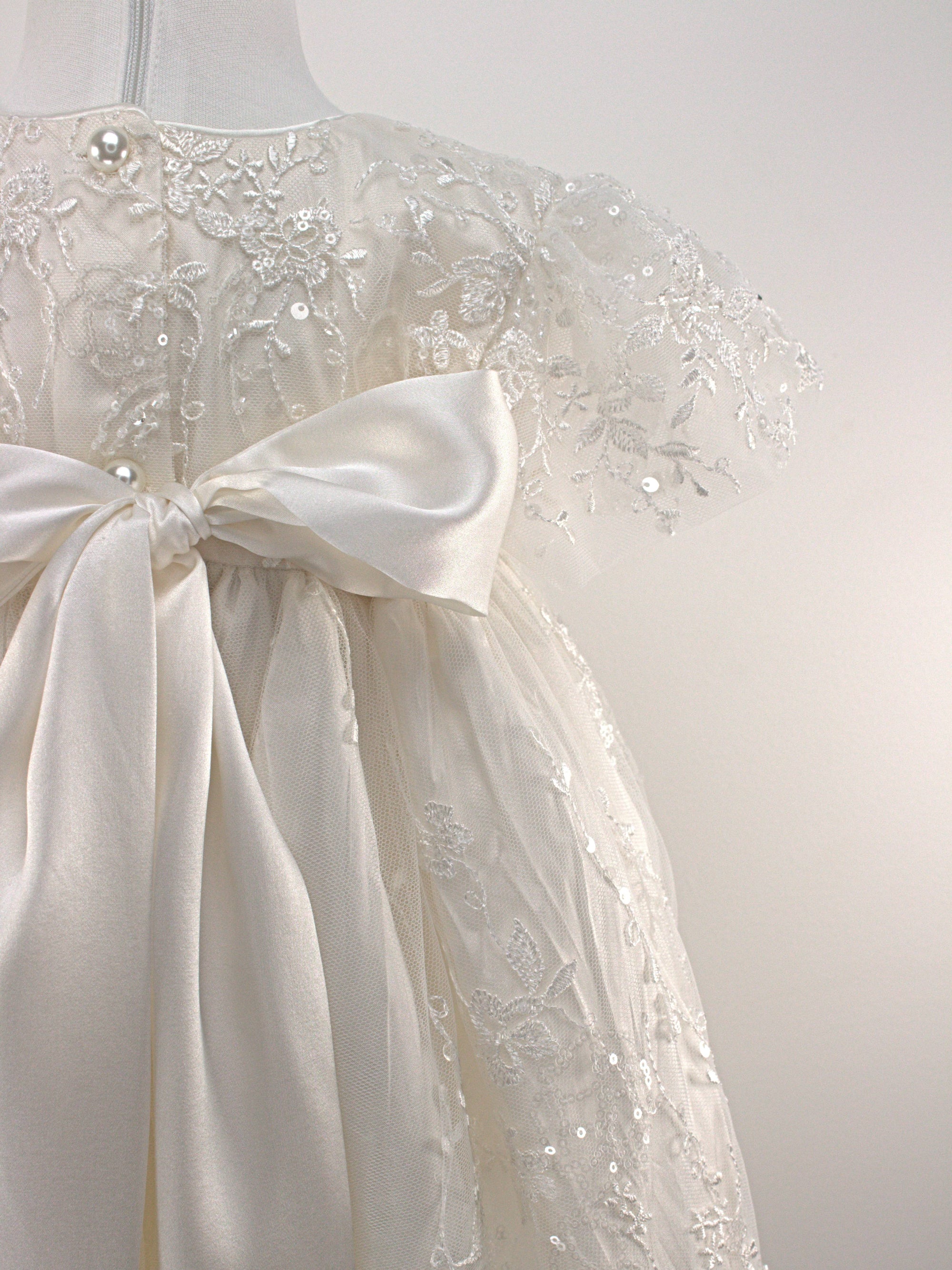 Back view of the My Blessing Eternal ivory christening gown showing lace detailing, back closures, and the smooth satin skirt.