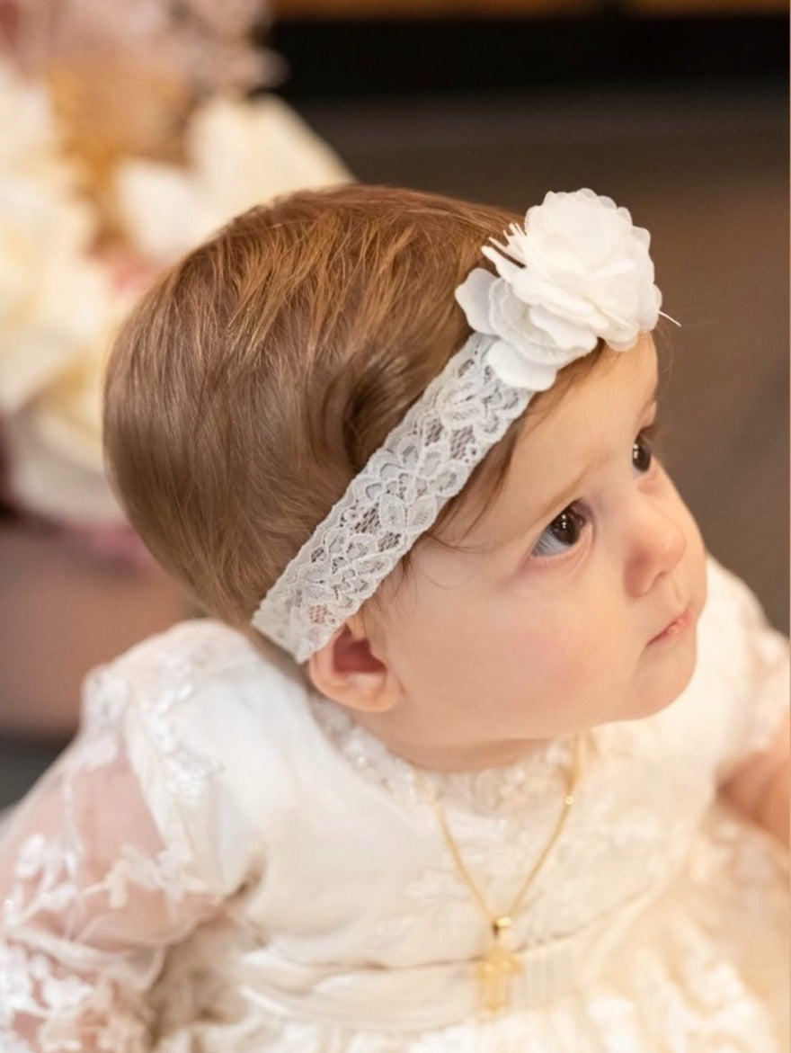 Baby girl wearing the My Blessing Faith christening gown with the floral lace overlay glowing softly in the natural light.