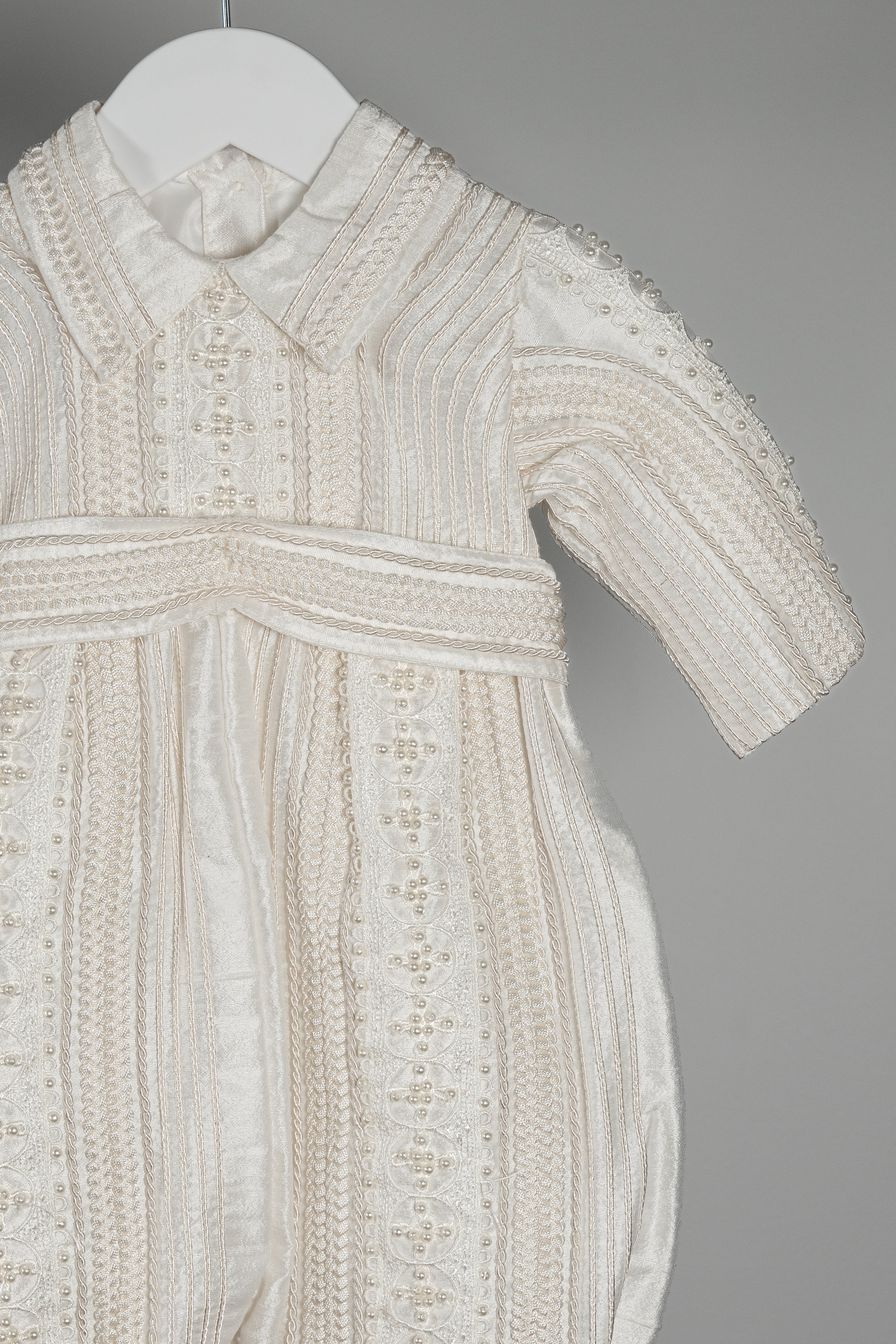 Macro shot of the My Blessing Gabriel romper’s Dupioni silk highlighting its natural texture and fine lace embellishment.