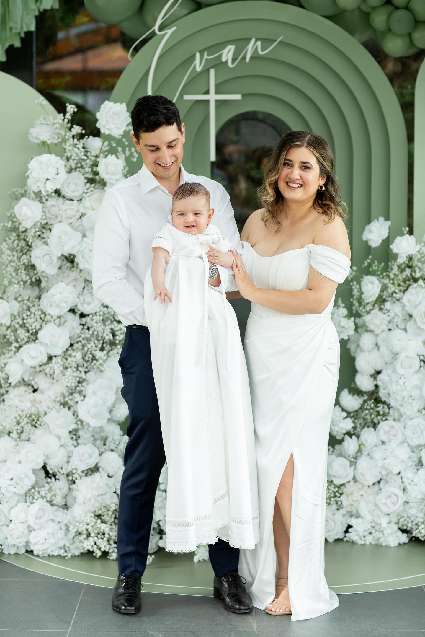 Mum and dad admiring their baby dressed in the My Blessing Georgie Mikado christening romper, the soft sheen of the fabric enhancing the moment.