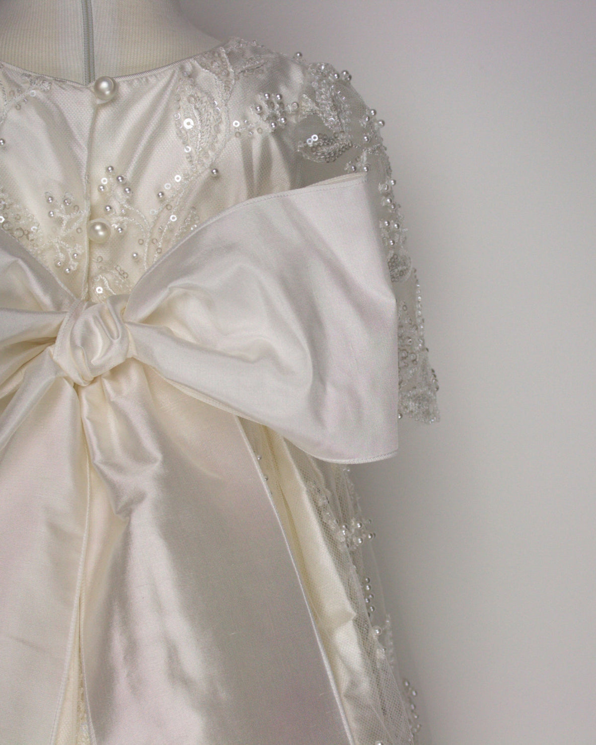 Close-up of the my Blessing Gianna gown’s back bodice featuring delicate lace patterns decorated with glass seed beads as well as pearls and large silk bow.
