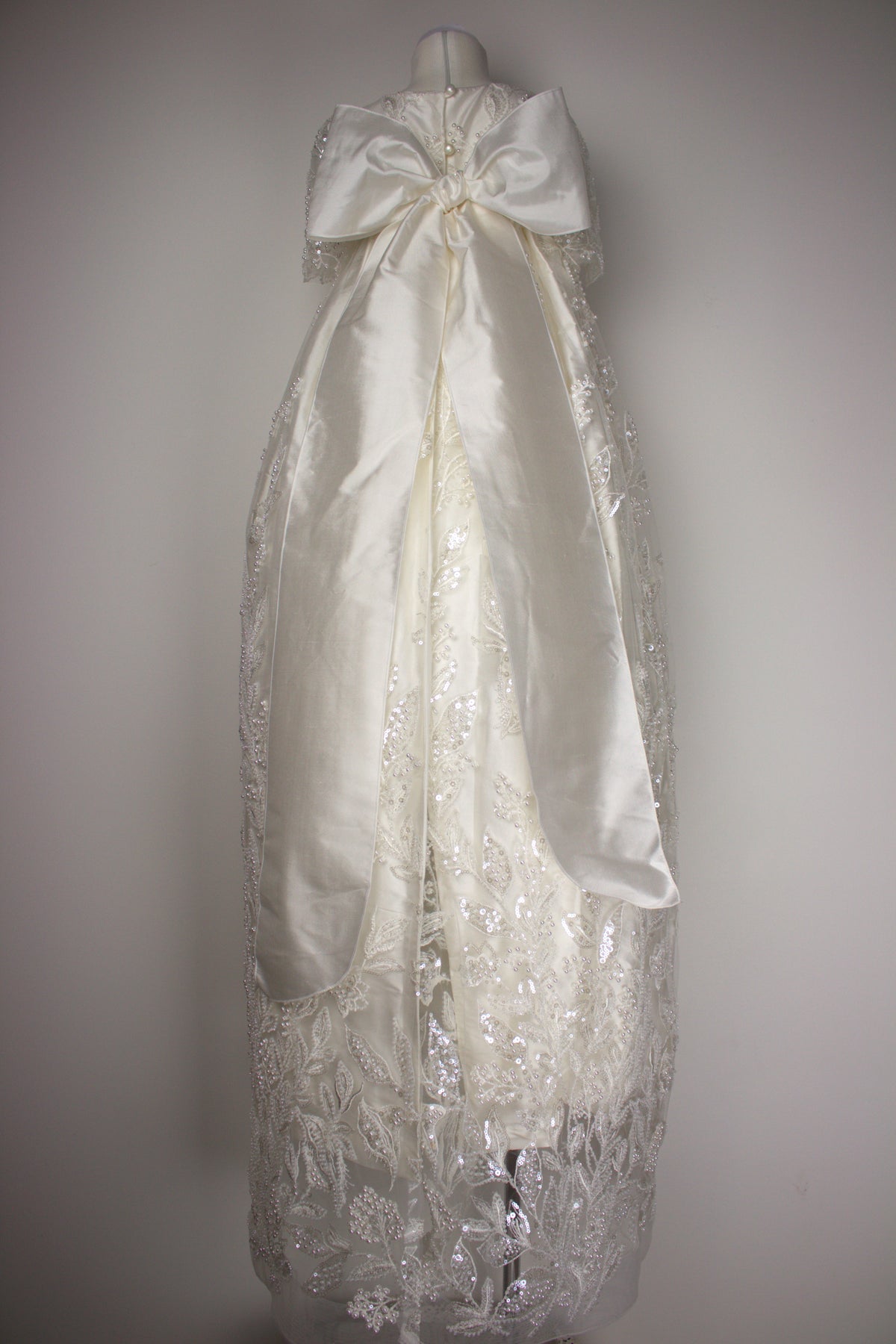 Back view of the My Blessing Gianna ivory christening gown showing embroidered lace detailing, soft flowing lace with bead and pearl accents completed with an extra-large pure silk bow.