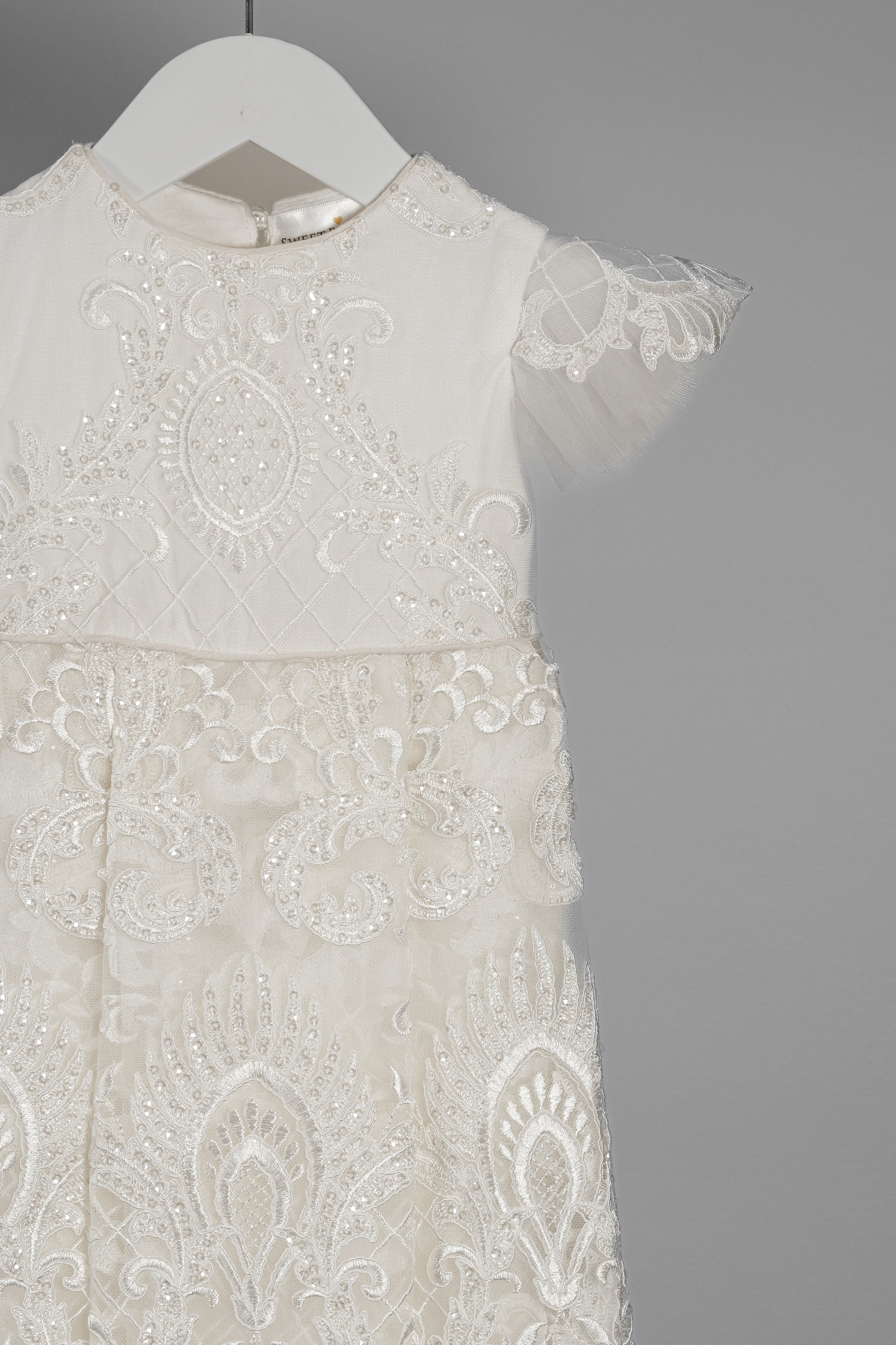 Close-up of the My Blessing Lilly christening gown’s front bodice showing intricate floral lace embroidery layered over a smooth cotton underlay.