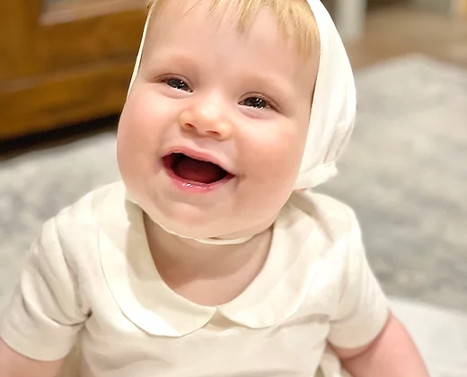 Close-up of the Noa christening gown showing the linen texture, Peter Pan collar, and baby boy smiling.