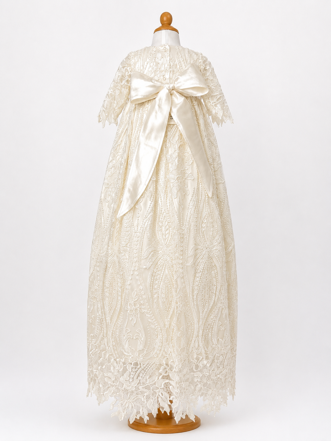 Back full length image of My Blessing Praise ivory lace and beaded christening gown featuring short lace sleeves, pearl button closures, a large silk bow at the back, and a lace-trimmed hem.