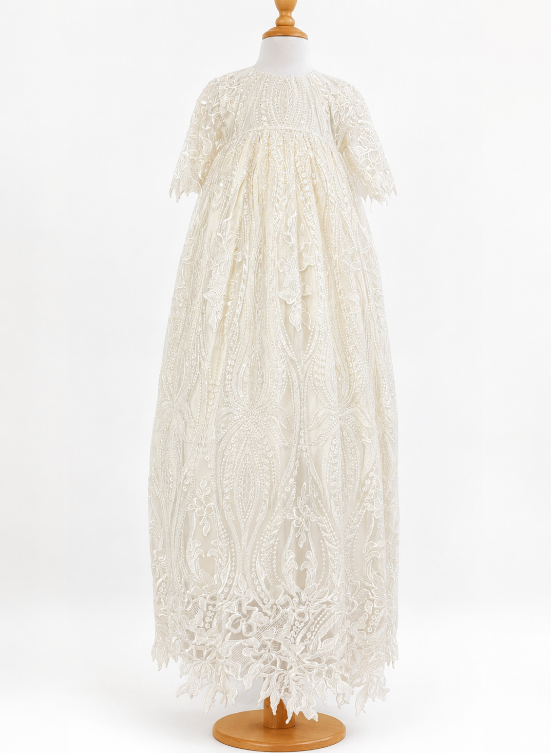 Front full length image of My Blessing Praise ivory lace and beaded christening gown displayed on a wooden dress form against a plain white studio background. The dress features a high neckline, short lace sleeves and a lace-trimmed hem.