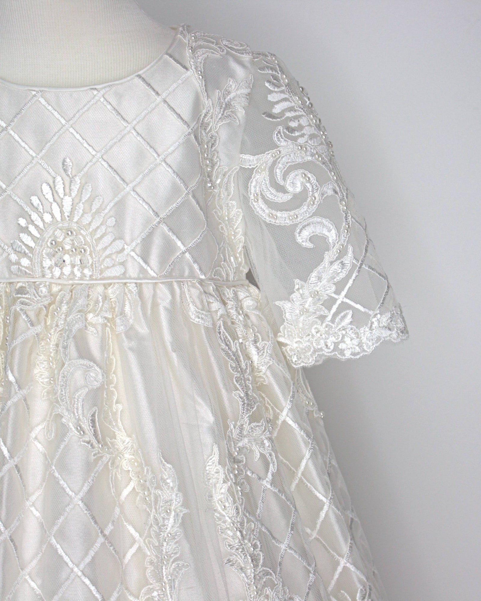 Close-up of the My Blessing Psalms christening gown’s front bodice showing intricate floral lace embroidery embellished with glass seed beads and pearl detailing.