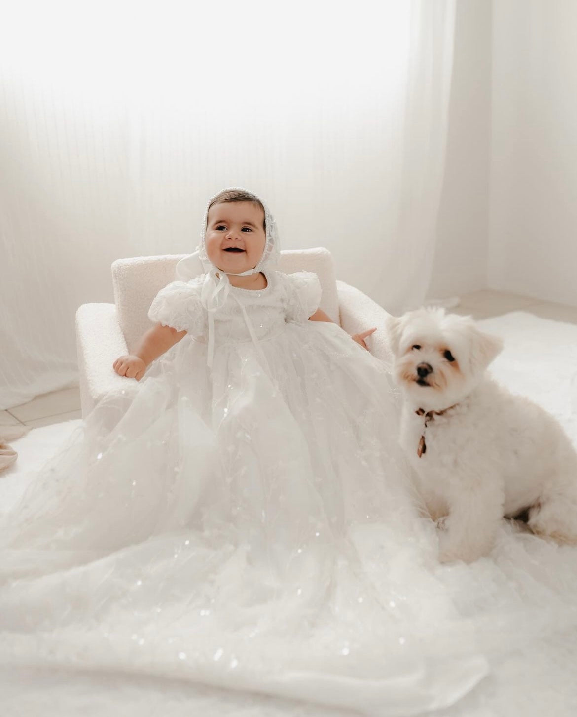 Baby girl seated beside a white fluffy puppy while wearing the My Blessing Shamiran Gown, captured in a soft lifestyle moment.