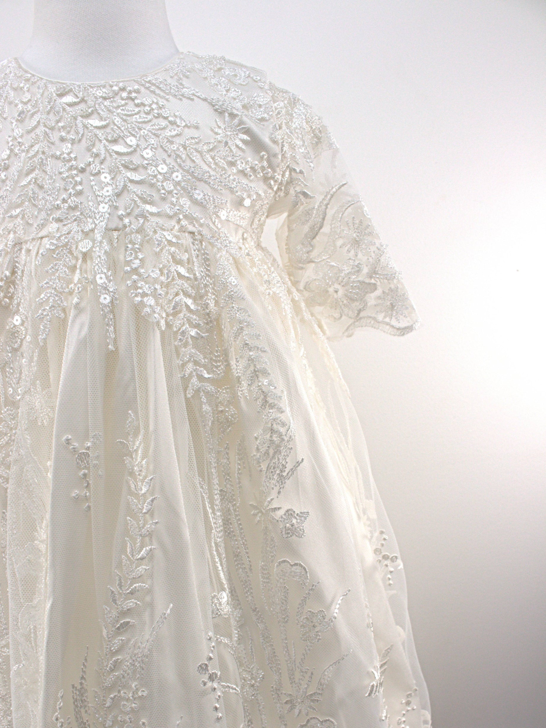 Close-up of the My Blessing Worthy christening gown’s front bodice showing detailed floral lace and bead embroidery.